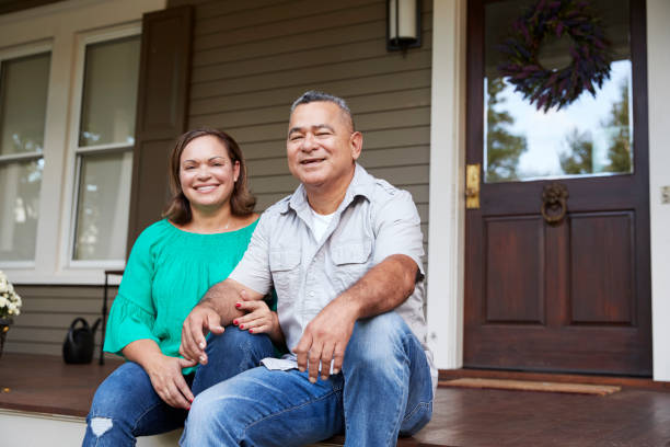 Portrait Of Smiling Senior Couple Sitting In Front Of Their Home
